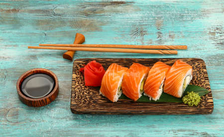 Close up one set of six Philadelphia sushi rolls with raw salmon served on palm wood plate on blue table, higgh angle viewの写真素材