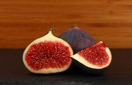 Close up one whole fresh ripe fig fruit with cut half and quarter slice on cutting board on table, low angle side viewの写真素材