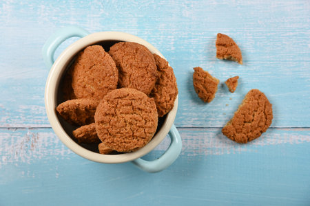 Close up round artisan oatmeal cookies in pannikin bowl on blue painted rustic wooden table,...