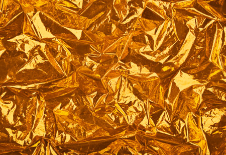 Close up festive abstract background of golden orange crumpled glossy metallic plastic foilの写真素材