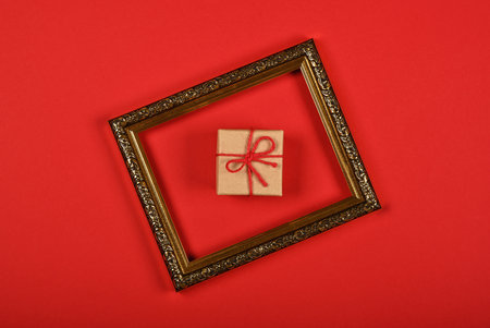 Close up one brown paper giftbox in golden frame over red background, flat lay, elevated top view, directly aboveの写真素材