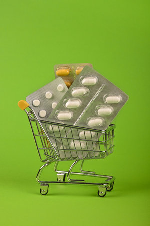 Close up several different blister packs of pills in small shopping cart over green background, concept of online medicine order delivery, low angle viewの写真素材