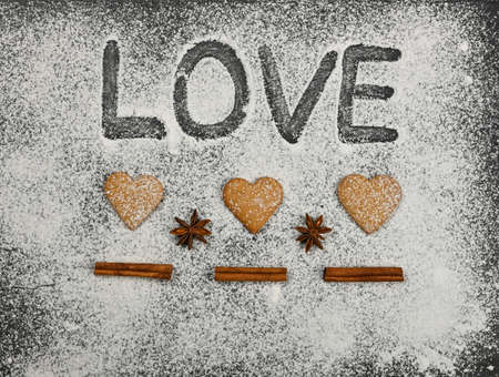 Close up three heart shaped gingerbread cookies on background of black slate with cinnamon and anise stars, LOVE word on powdered white sugar icing and copy space, elevated top view, directly aboveの写真素材