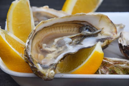 Close up portion of fresh open raw juicy oysters with lemon wedges on white plastic tray on a table, high angle viewの写真素材