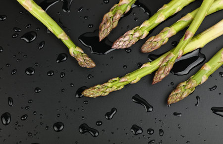 Close up bunch of washed fresh green asparagus on black table with drops of water, elevated top view, directly aboveの写真素材