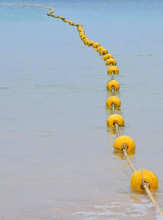 Chain of yellow polystyrene sea marker buoys with cable tow in blue sea water, in perspectiveの写真素材