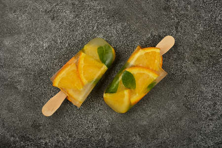 Close up two fruit ice cream with fresh orange slices and green mint leaves on gray table surface, elevated top view, directly aboveの写真素材