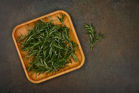 Close up fresh green rosemary leaves on bamboo wooden plate on table, elevated top view, directly aboveの写真素材