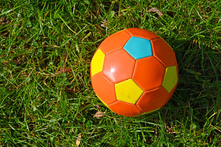 Close up one orange multicolor childish soccer football ball in green grass of turf meadow,...