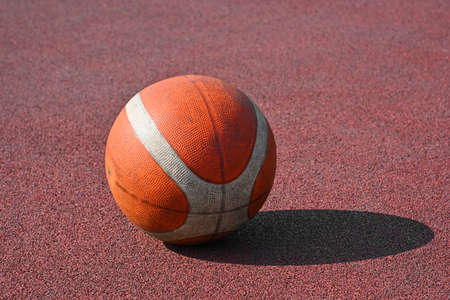 Close up one orange colored unbranded basketball ball over red outdoors court background, high angle viewの写真素材