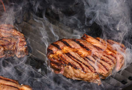 Close up searing and smoking ribeye beef steaks on open fire outdoor grill with cast iron metal grate, high angle viewの写真素材