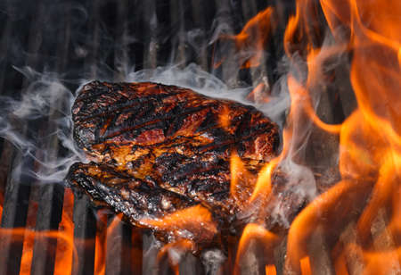 Close up searing and smoking ribeye beef steaks on open fire outdoor grill with cast iron metal grate, high angle viewの写真素材