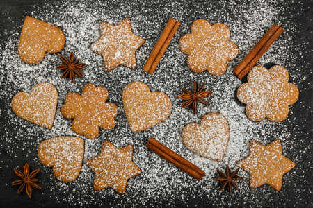 Close up heart and star shaped Christmas gingerbread cookies with cinnamon and star anise spices on black slate background with powdered white sugar icing, elevated top view, directly aboveの写真素材