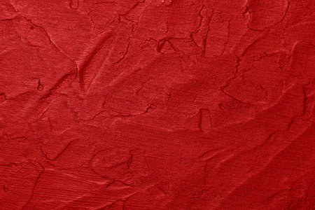 Close up vivid scarlet red abstract background texture of uneven grunge surface with brushstrokes of plaster and paintの写真素材