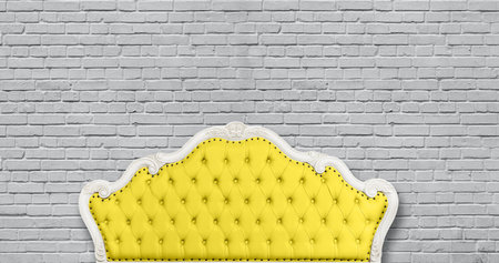 One yellow leather capitone chesterfield sofa headboard on background of gray painted brick wall...