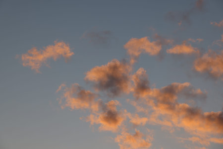 Beautiful cloudscape with brightly lit pink and orange fluffy early sunset clouds over blue sky, low...
