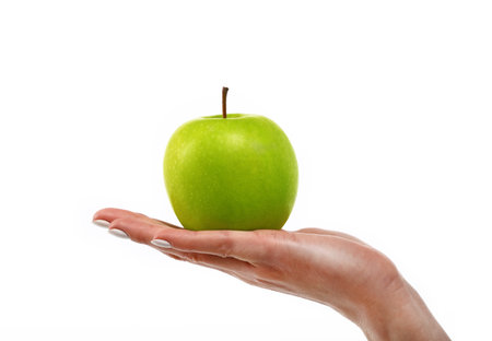 Close up Caucasian woman hand holding one fresh green apple isolated on white background, symbol of healthy eating concept, low angle, side viewの写真素材