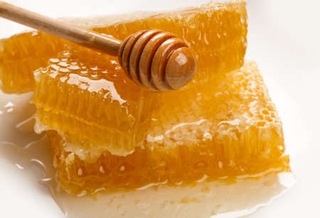 Close up stack of several fresh cut golden comb honey slices and natural wooden dipper on plate isolated on white background, high angle viewの写真素材
