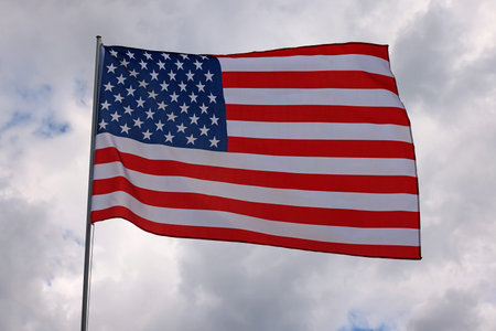 US national flag flying and waving in the wind over gray stormy cloudy sky, symbol of American...