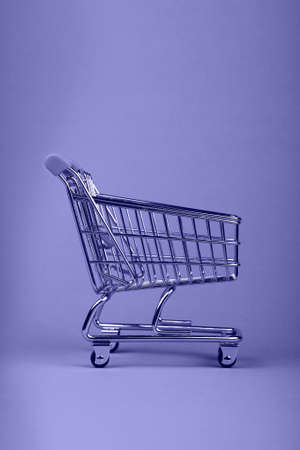 Close up empty toy metal supermarket shopping cart over lavender background with copy space, very peri, color of year 2022の写真素材