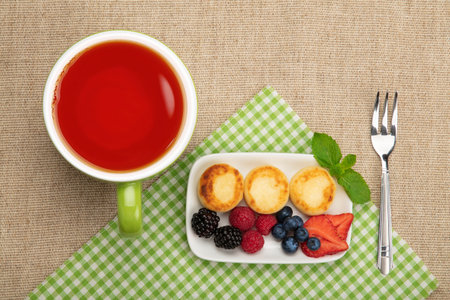 Close up serving portion of European quark cheese pancakes dessert with fruits and cup of red black tea, elevated top view, directly aboveの写真素材