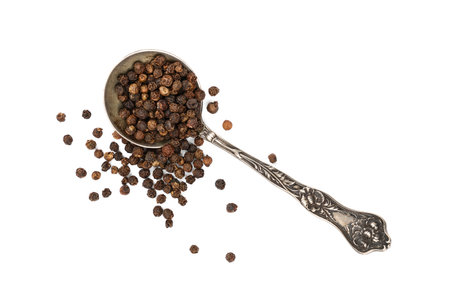 Close up one vintage metal spoon full of black pepper peppercorns and heap of peppercorns spilled...