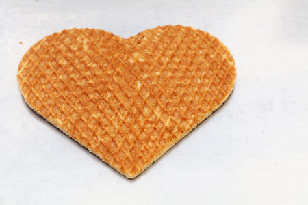 Close up one heart shaped traditional sweet Dutch stroopwafel (syrup waffle) cookie on white baking paper, high angle viewの写真素材