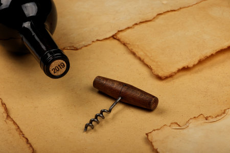 Close up one full unopen bottle of red wine with cork and retro opener with wooden handle over...
