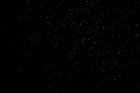 Close up white snow falling over black background of night winter sky in the darkの写真素材