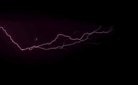 Flash of lightning bolt in stormy black night sky during thunderstorm, copy space