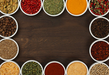 Frame of assorted spices in white ceramic bowls over dark wooden table background with copy space, elevated top view, directly aboveの写真素材