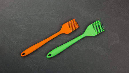 Two silicone brushes for pastry or basting on black slate board with copy space, colorful modern culinary kitchen utensils, close up, elevated table top view, directly aboveの写真素材
