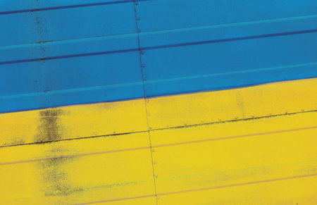 Grunge weathered national flag of Ukraine over studded steel armor metal surface background, symbol of Ukrainian patriotismの写真素材