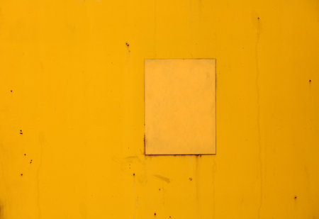 Close up of a vibrant yellow metal surface featuring a lighter square patch, revealing signs of aging, wear, rust stains, and scattered imperfections for a textured, industrial lookの写真素材