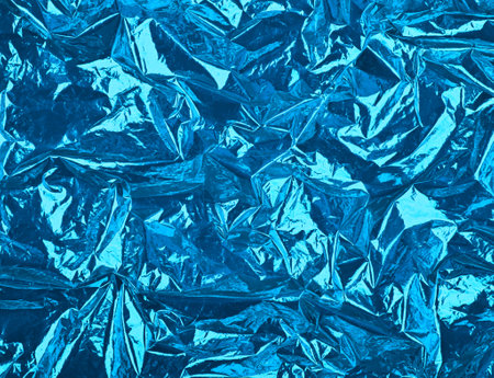 Close up festive abstract background of blue crumpled glossy metallic plastic foilの写真素材