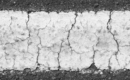 Close up view of a weathered and cracked white traffic line dividing a dark asphalt road, showcasing the contrasting textures and the effects of time and usage on road markingsの写真素材