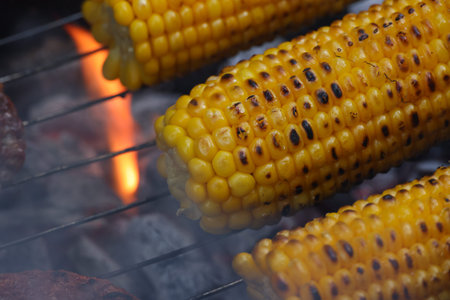 Grilling delicious corn on the cob on BBQ grill grate, creating a mouthwatering summer meal. Flames...