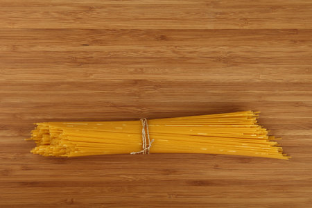 Bundle of uncooked dry spaghetti tied with string, resting on a wooden cutting board, ready for cooking and italian cuisine preparation, top down viewの写真素材