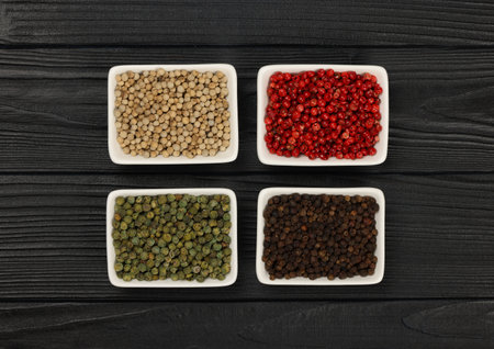 White ceramic bowls of assorted peppercorns, black, green, pink, white over dark wooden table background with copy space, elevated top view, directly aboveの写真素材