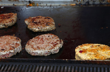 Gloved hands cooking burgers and veggie burgers on a hot grill, using a spatula to flip them over for even cookingの写真素材
