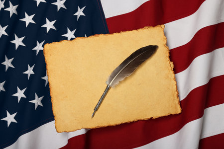 Close up blank old vintage yellow paper sheet and quill on cotton embroidered US national flag background, symbol of American history, elevated high angle view, directly aboveの写真素材