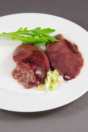 Raw chicken liver with vegetables at white plateの写真素材