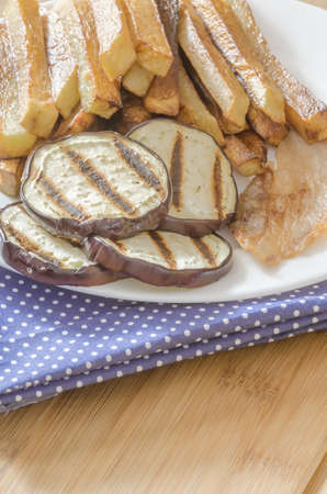 Fries potatoes with grilled eggplant on wooden backgroundの写真素材