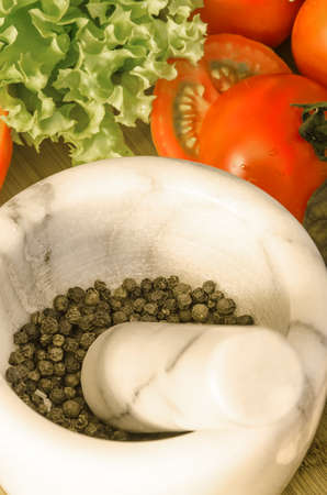 Marble mortar with pepper and vegetables on wooden tableの写真素材