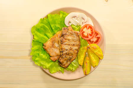 Grilled meat dish with tomato, potatoes and mushrooms on wooden backgroundの写真素材