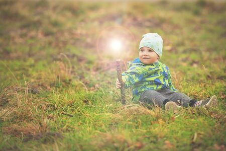 Small boy is sitting on grass and holding magic wand with light out of itの写真素材