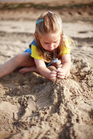 Cute kid playing with sand on a beachの写真素材