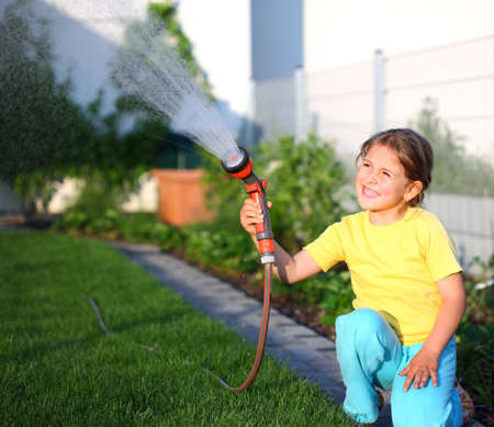 Little girl watering the grass in the gardenの写真素材