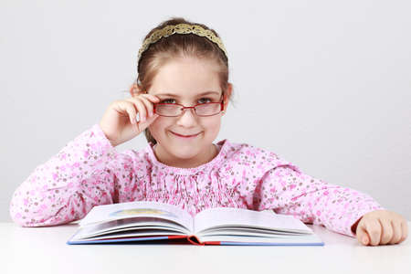 Cute schoolgirl with glasses reading bookの写真素材