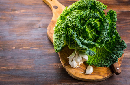 Fresh raw savoy cabbage with garlic and knife on wooden background